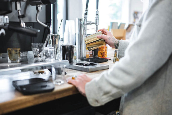 Barista washing a frothing milk pitcher with a Barista Basics rinser in a cafe