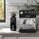 Ascaso coffee machine and Baratza grinder on a kitchen counter with a window and plants in the background
