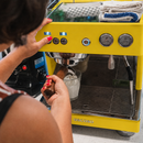 Person operating a yellow espresso machine with a focus on the brand 'Ascaso'.