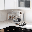 Modern kitchen with coffee machine, cups, and cookware on a white countertop.
