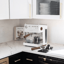 White espresso machine on a kitchen counter with black cabinets and marble countertop.